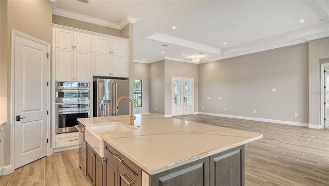 kitchen with a sink, white cabinetry, light wood-style floors, appliances with stainless steel finishes, and a center island with sink