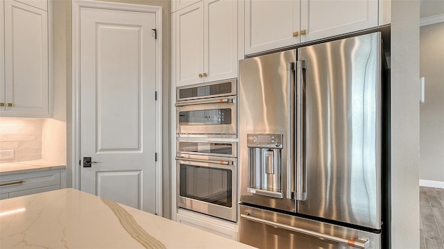 kitchen featuring light stone counters, stainless steel appliances, wood finished floors, white cabinets, and decorative backsplash