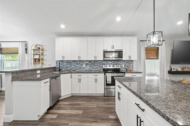 kitchen featuring appliances with stainless steel finishes, tasteful backsplash, decorative light fixtures, dark stone countertops, and dark hardwood / wood-style flooring