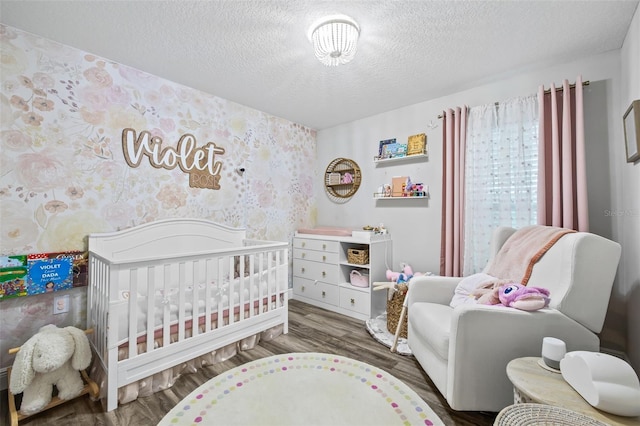 bedroom with a crib, dark wood-type flooring, and a textured ceiling