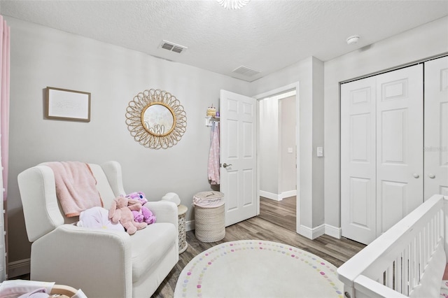 bedroom featuring a textured ceiling, a nursery area, wood-type flooring, and a closet