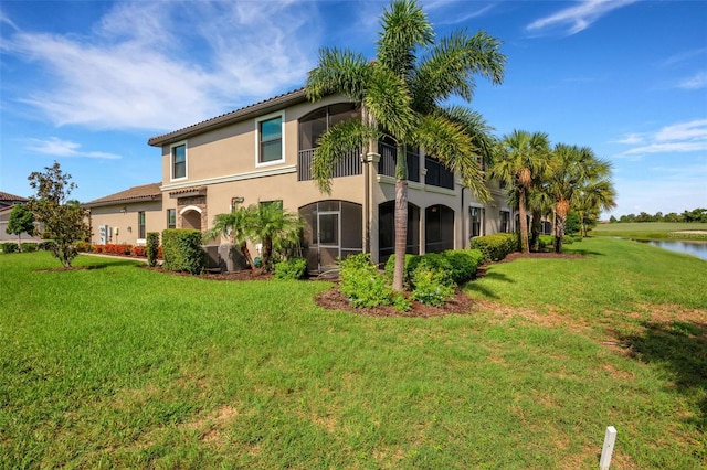 back of property with a lawn, a water view, and a sunroom