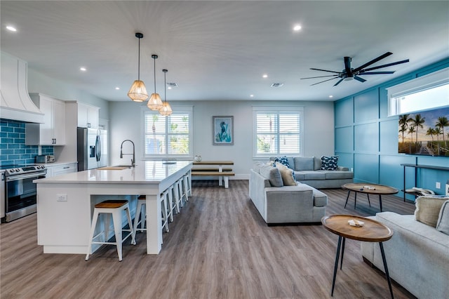 kitchen with white cabinetry, hanging light fixtures, stainless steel appliances, backsplash, and an island with sink