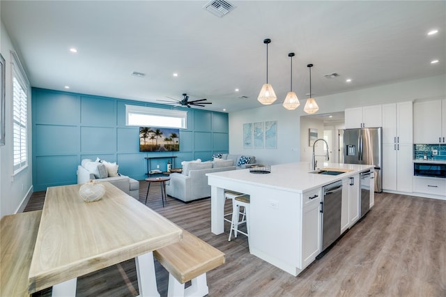 kitchen featuring a kitchen island with sink, white cabinets, ceiling fan, decorative light fixtures, and stainless steel appliances