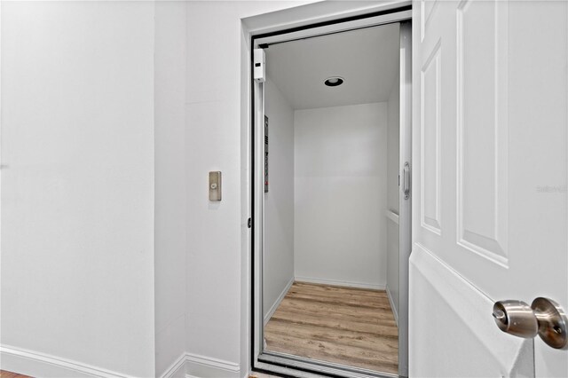 interior space with elevator, baseboards, and wood finished floors