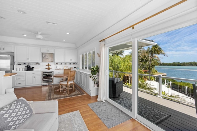 living room with beverage cooler, light hardwood / wood-style floors, a water view, and ceiling fan