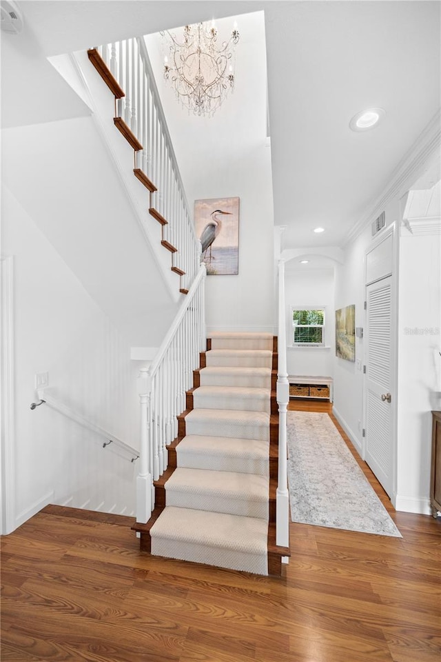 stairway featuring an inviting chandelier, crown molding, and hardwood / wood-style floors