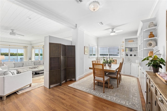 dining room with light wood finished floors, baseboards, a ceiling fan, ornamental molding, and a water view