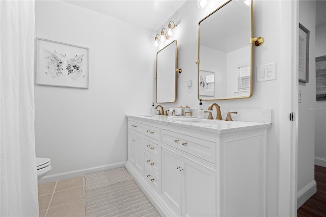 bathroom with toilet, a sink, baseboards, tile patterned floors, and double vanity