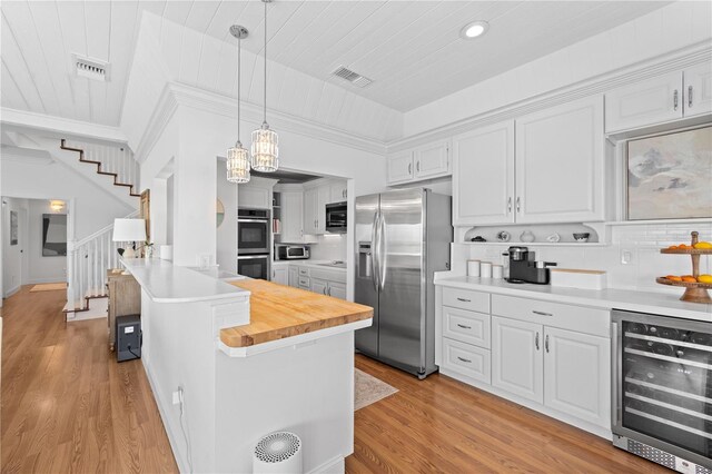 kitchen featuring beverage cooler, pendant lighting, white cabinets, light wood-type flooring, and appliances with stainless steel finishes