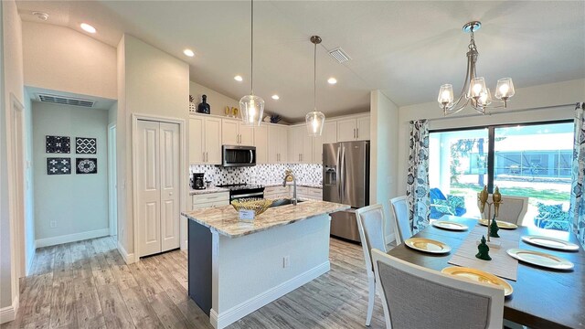 kitchen with backsplash, an island with sink, white cabinets, appliances with stainless steel finishes, and lofted ceiling