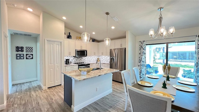 kitchen featuring vaulted ceiling, appliances with stainless steel finishes, decorative light fixtures, an island with sink, and white cabinets