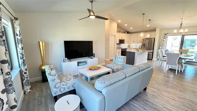 living room featuring ceiling fan with notable chandelier, high vaulted ceiling, and light hardwood / wood-style flooring