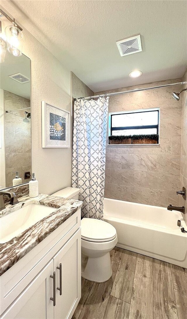 full bathroom with shower / tub combo with curtain, wood-type flooring, a textured ceiling, vanity, and toilet