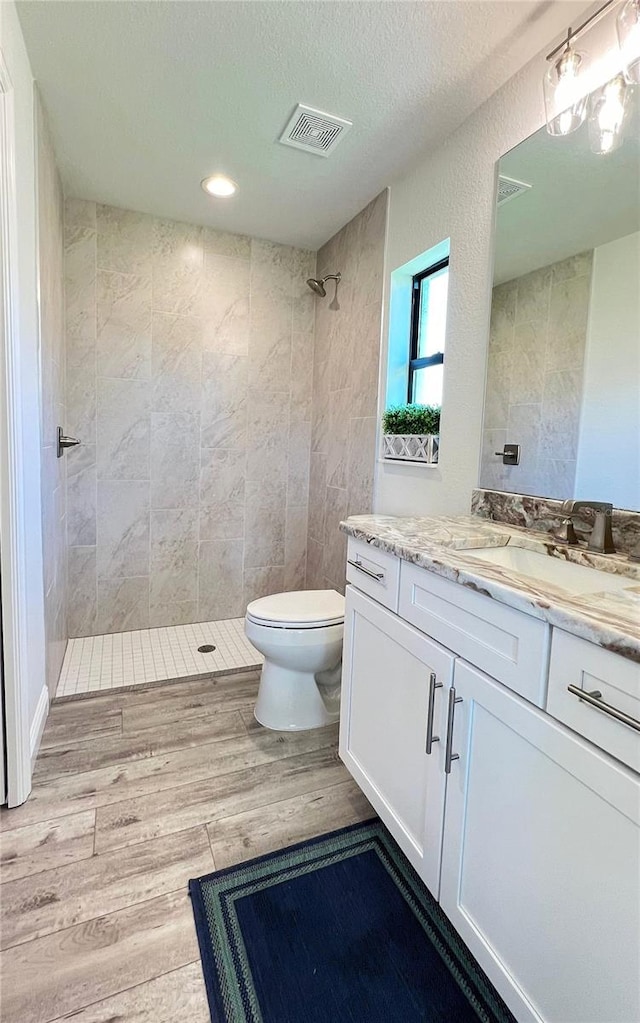 bathroom with toilet, a tile shower, vanity, and a textured ceiling