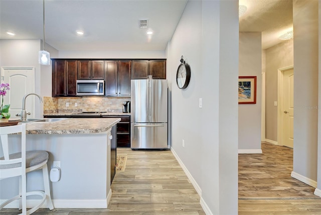 kitchen with appliances with stainless steel finishes, decorative light fixtures, sink, a kitchen bar, and dark brown cabinetry