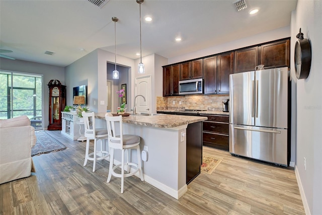 kitchen featuring appliances with stainless steel finishes, decorative light fixtures, sink, backsplash, and a kitchen island with sink