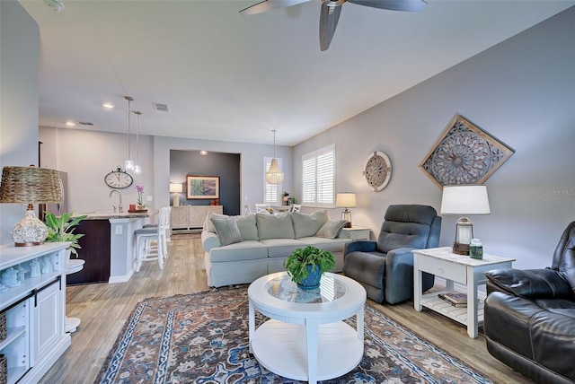 living room with ceiling fan, sink, and light wood-type flooring