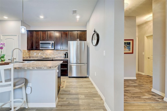 8930 Tuscany Isles Dr, Punta Gorda, FL 33950 - kitchen featuring stainless steel appliances, light wood-type flooring, dark brown cabinets, light countertops, and tasteful backsplash