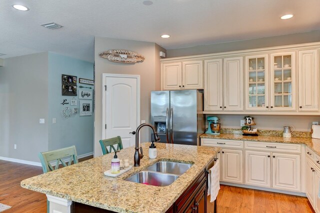 kitchen featuring stainless steel fridge, sink, light stone counters, light hardwood / wood-style floors, and an island with sink