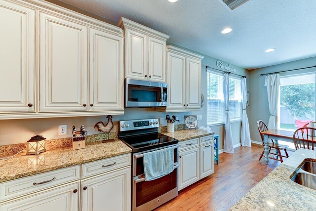 kitchen with white cabinetry, stainless steel appliances, light hardwood / wood-style floors, and light stone countertops