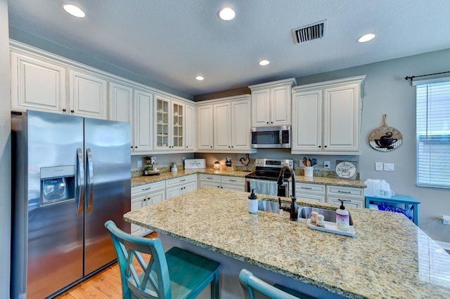 kitchen with white cabinetry, light stone counters, light wood-type flooring, and stainless steel appliances