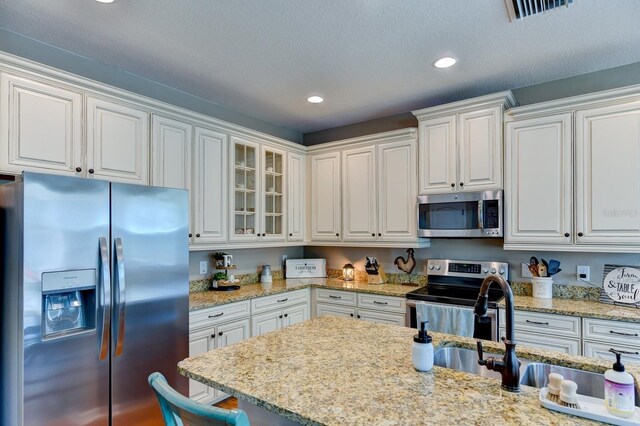 kitchen with white cabinetry, a textured ceiling, stainless steel appliances, light stone countertops, and sink