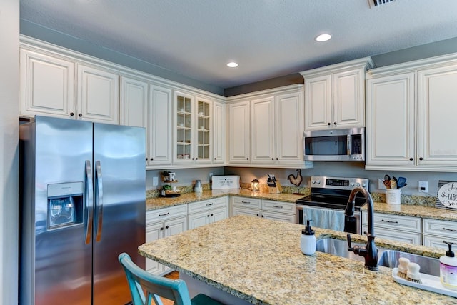 kitchen with a textured ceiling, white cabinets, light stone counters, stainless steel appliances, and sink