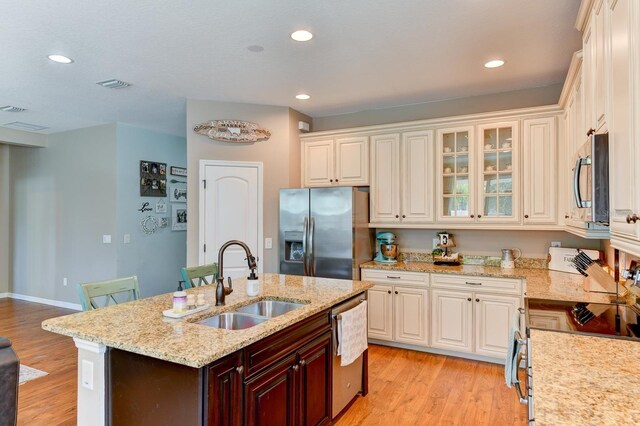 kitchen with light hardwood / wood-style floors, sink, an island with sink, and stainless steel appliances