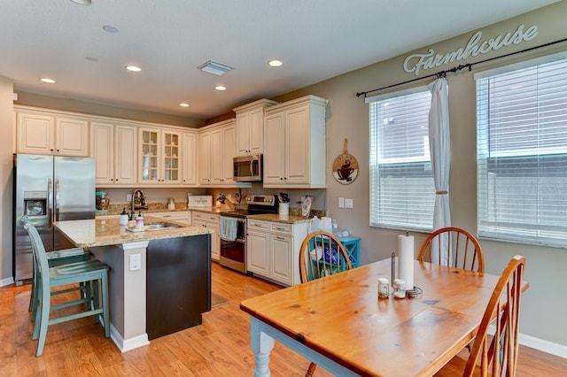 kitchen featuring appliances with stainless steel finishes, sink, light hardwood / wood-style floors, a kitchen island with sink, and light stone countertops