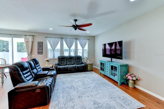 living room with a textured ceiling, ceiling fan, and light wood-type flooring