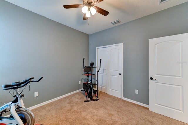 exercise room with light colored carpet and ceiling fan