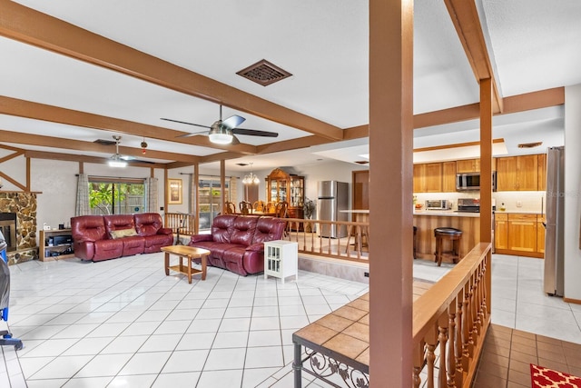 living room featuring light tile patterned floors, a stone fireplace, beamed ceiling, and ceiling fan