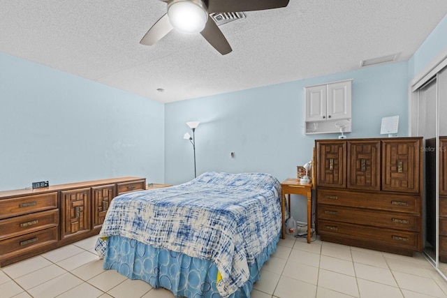 tiled bedroom with a textured ceiling, ceiling fan, and a closet