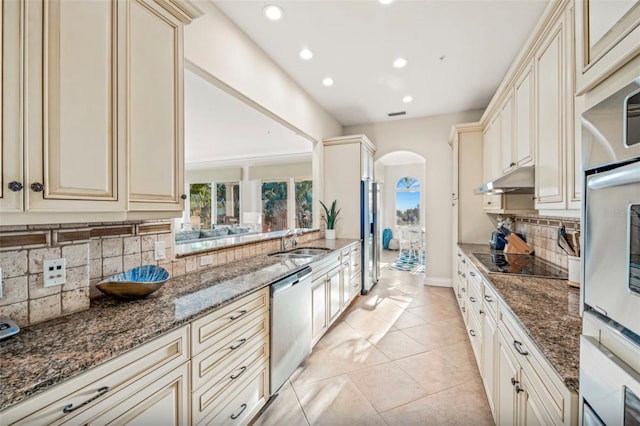 kitchen featuring black electric stovetop, dishwasher, cream cabinetry, and dark stone counters