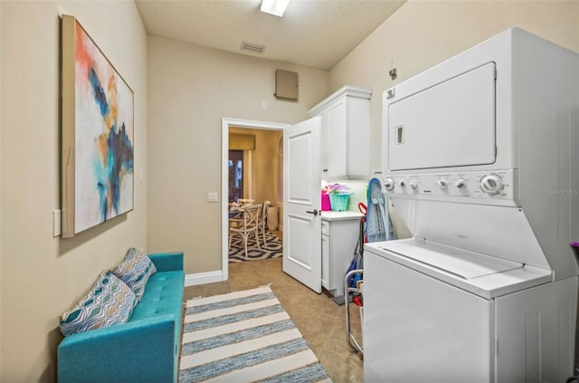 washroom featuring light tile patterned floors, stacked washer and dryer, a textured ceiling, and cabinets