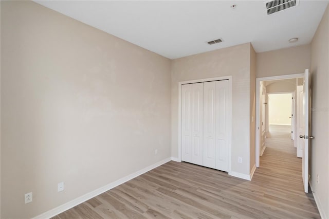 unfurnished bedroom featuring light wood-style floors, visible vents, a closet, and baseboards