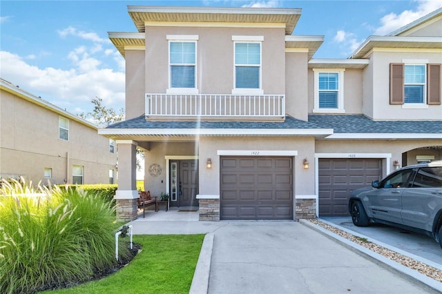 townhome / multi-family property with stucco siding, stone siding, a balcony, and roof with shingles