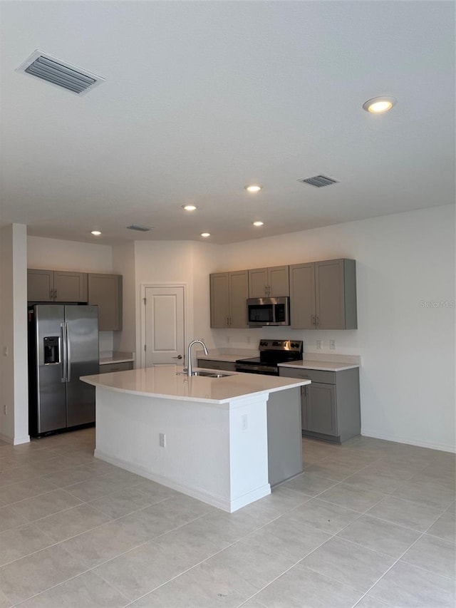 kitchen with light tile patterned floors, stainless steel appliances, gray cabinetry, a kitchen island with sink, and sink