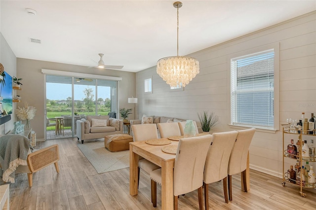 dining area featuring ceiling fan with notable chandelier, wooden walls, and light hardwood / wood-style floors