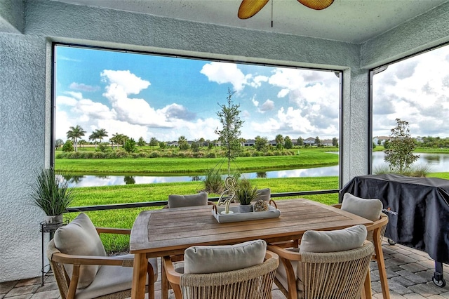 sunroom with ceiling fan and a water view