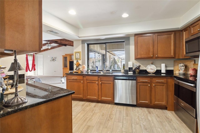 kitchen with stainless steel appliances, vaulted ceiling, sink, light hardwood / wood-style flooring, and dark stone countertops