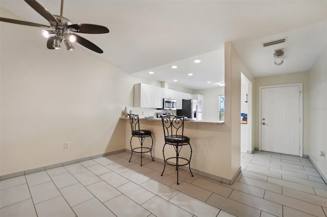 kitchen featuring kitchen peninsula, appliances with stainless steel finishes, a breakfast bar, ceiling fan, and white cabinets