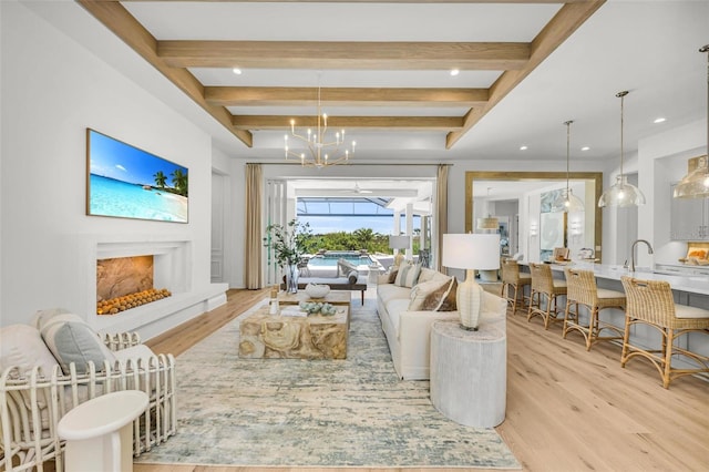 living room featuring sink, beam ceiling, a chandelier, and light wood-type flooring