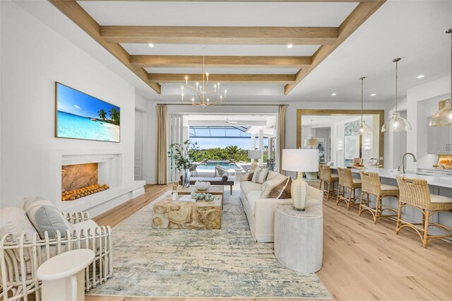 living room featuring sink, beam ceiling, a chandelier, and light wood-type flooring