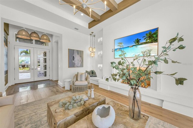 living room featuring a chandelier, wood-type flooring, beam ceiling, and french doors