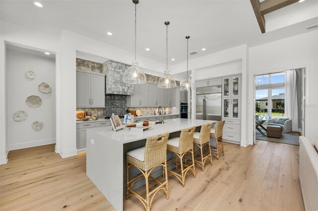 kitchen featuring built in refrigerator, gray cabinetry, a large island, and a breakfast bar area