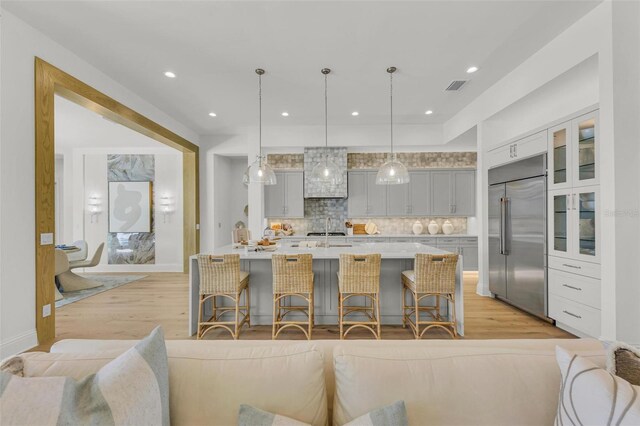 kitchen with tasteful backsplash, stainless steel built in fridge, hanging light fixtures, a breakfast bar area, and gray cabinets