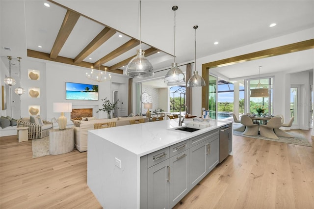 kitchen with pendant lighting, an island with sink, sink, gray cabinets, and light wood-type flooring