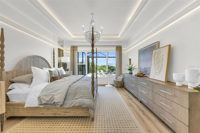 bedroom with access to exterior, a chandelier, light hardwood / wood-style flooring, and a tray ceiling